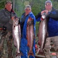 Three men holding up fish while standing on a dock.