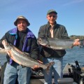 Two men holding up fish on a boat.