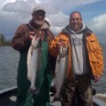 Two men holding fish while standing on a boat.