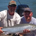 Two men holding a fish while standing on the water.