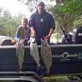 Two men holding fish on a boat in the water.