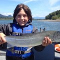 A young boy holding up a fish on top of a boat.