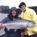 Two men holding a fish while standing on the side of a boat.