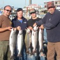 Four people holding up fish on a boat.