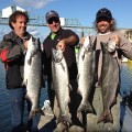 Three men holding up four fish on a boat.