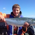 A boy holding a fish while sitting on the boat.