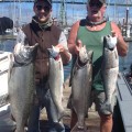 Two men holding up large fish on a boat.