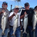 Four men holding up fish on a boat.