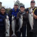 Four people holding up fish on a boat.