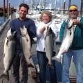 Three people holding up fish on a dock.