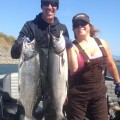 A man and woman holding two fish on top of a boat.