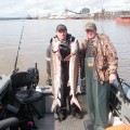 Two men standing on a boat with fish.