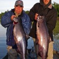 Two men holding up large fish on a boat.