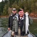 Two men in a boat holding fish on the water.