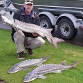 A man holding two fish in front of a boat.