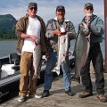 Three men standing on a dock holding fish.