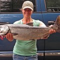 A woman holding a large fish in front of a blue van.