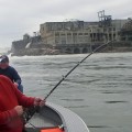 A man fishing from the water while another man watches.