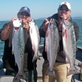 Two men holding up large fish on a boat.