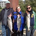 Three people holding up fish on a dock.