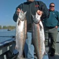 Two men holding up large fish on a boat.