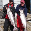 Two men holding up large fish on a dock.