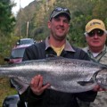 Two men holding a large fish in front of trees.