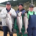 Three people holding up fish on a dock.