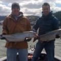 Two men holding up fish on a boat.