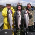 Three men holding up fish on a boat.